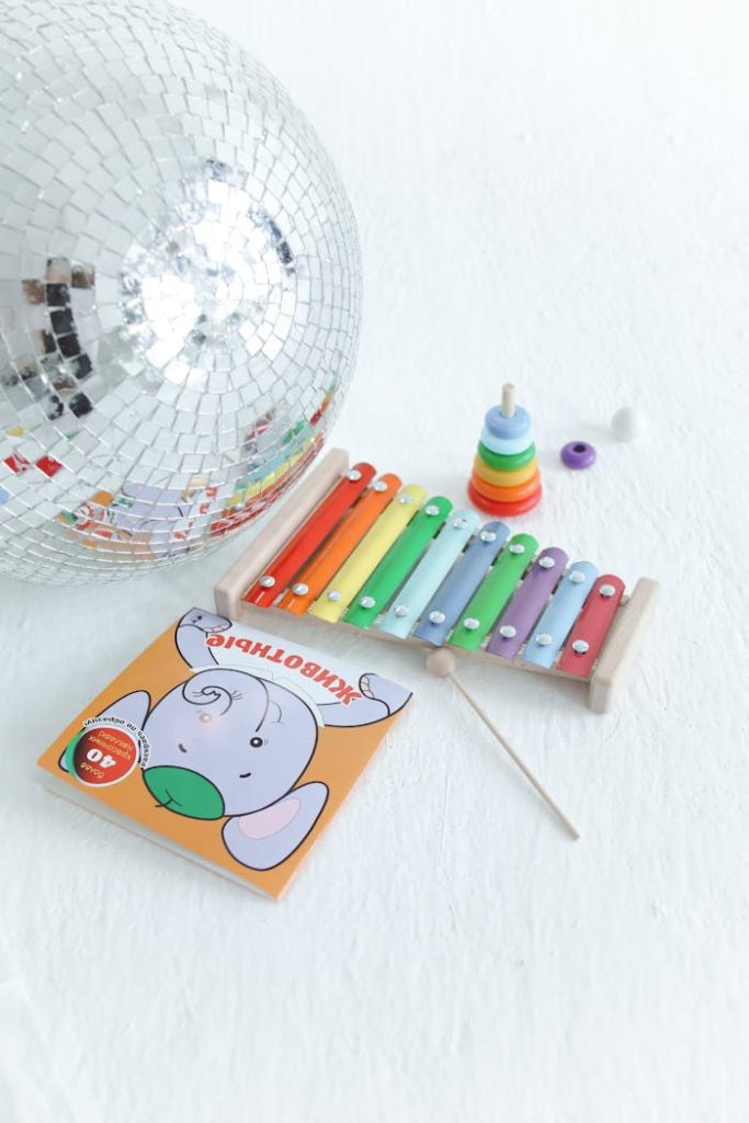 A collection of colorful childrens toys including a xylophone and disco ball on a white surface.